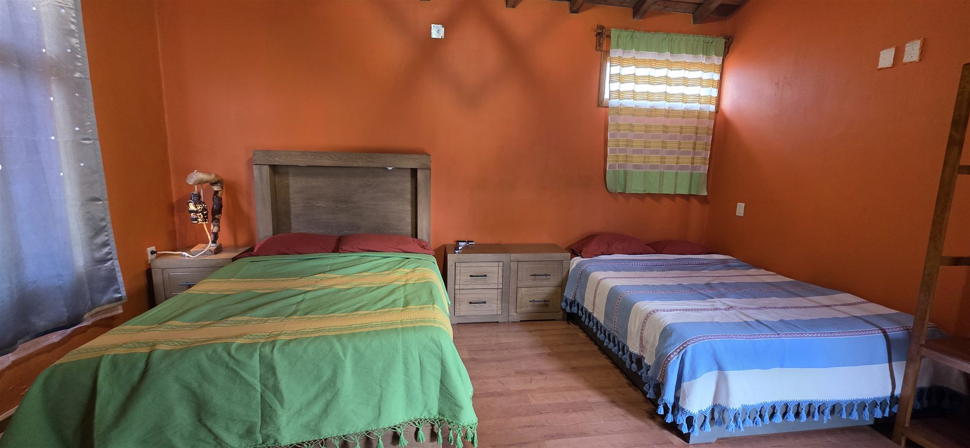 Interior de la cabaña con dos camas, textiles oaxaqueños y piso de madera