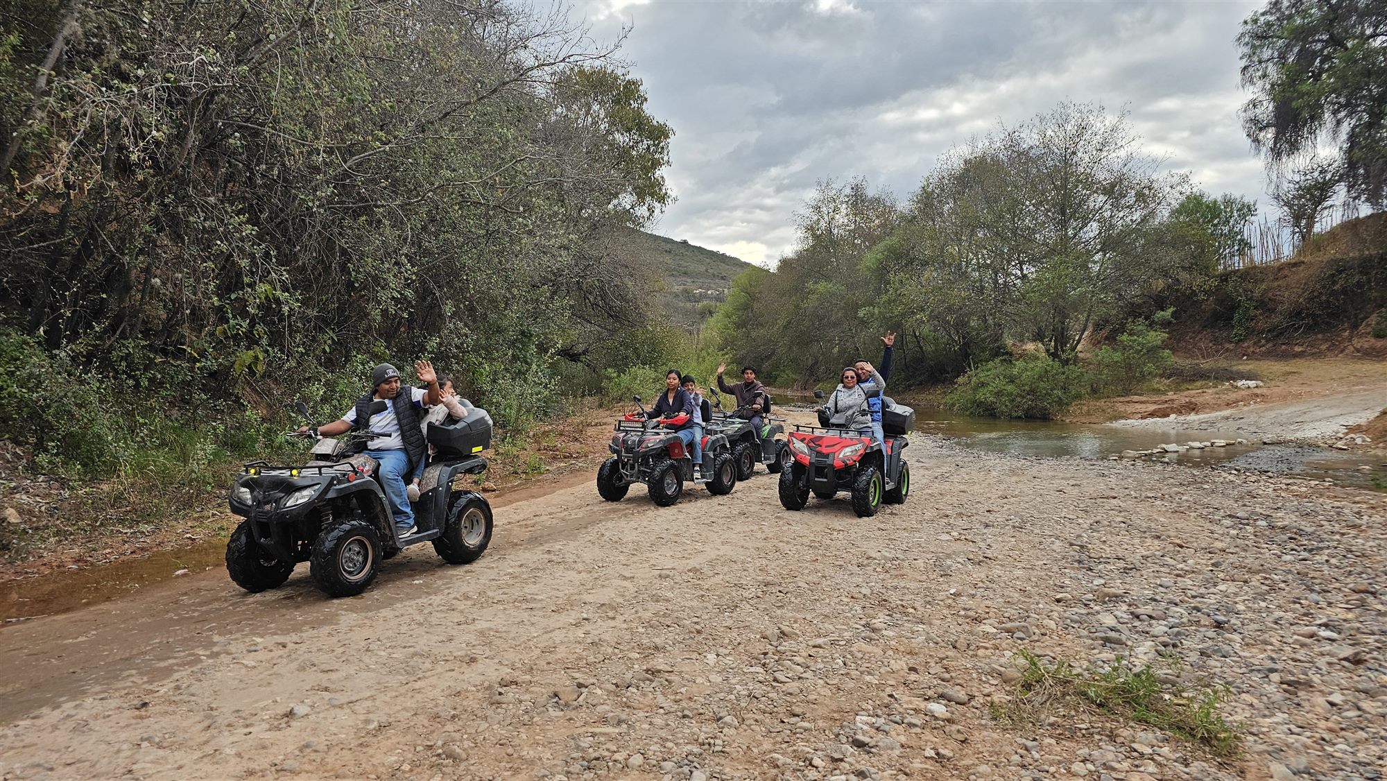 Familias en cuatrimotos sobre un camino de terracería junto al arroyo